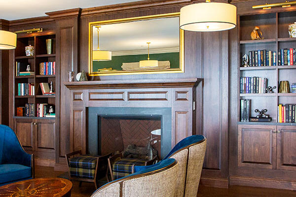 Resident lounge and library with built-in bookshelves, fireplace, comfortable seating, and warm wood finishes.