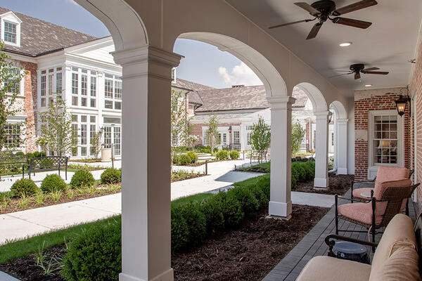 Covered outdoor courtyard at an independent living community featuring brick architecture, landscaped walkways, shaded seating, and resident gathering spaces.