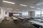 Modern large classroom containing rows of wood finished tables and rolling chairs 