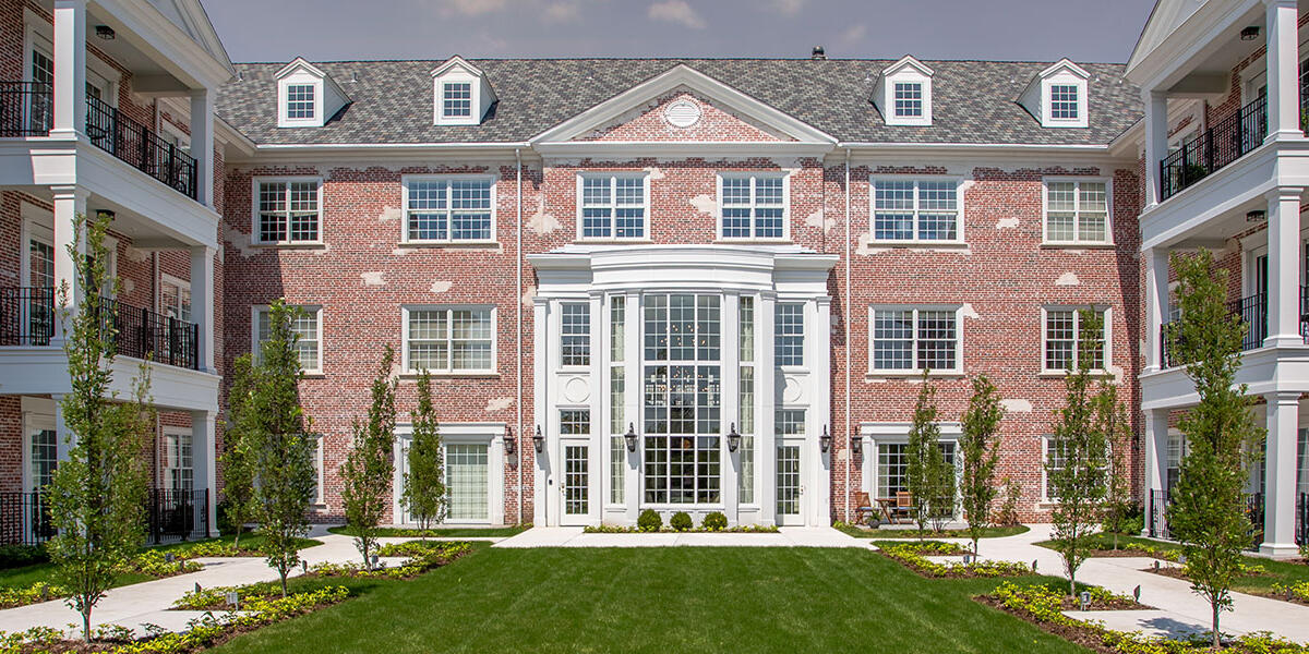 Three-story independent living residence with brick façade, landscaped courtyard, balconies, and main entrance.