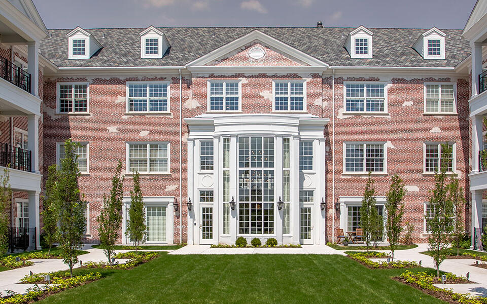 Three-story independent living residence with brick façade, landscaped courtyard, balconies, and main entrance.